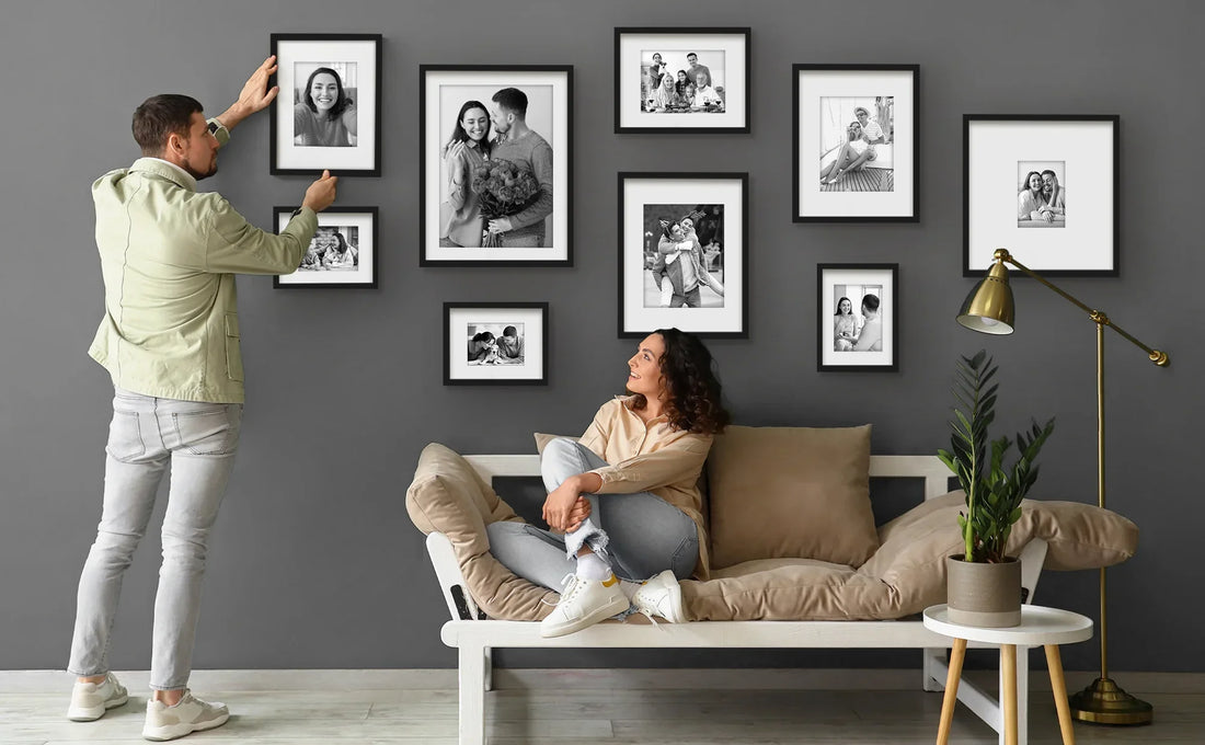 Man hanging framed family photos on gray wall.