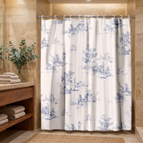 Shower curtain of blue toile pastoral scenes on cream in a wood and stone bathroom beside folded towels 