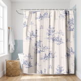 Shower curtain of blue toile pastoral scenes on cream in a bright white bathroom beside a tub and basket 