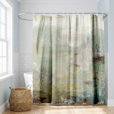 Abstract shower curtain in sage, teal and grey washes in a bright white bathroom beside a tub and basket 