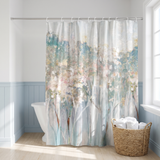 Abstract shower curtain of misty blossom trees in blush and teal in a bright white bathroom beside a tub and basket 