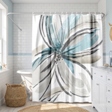 Shower curtain with a large brushed flower in teal and grey in a bright white bathroom beside a tub and basket 
