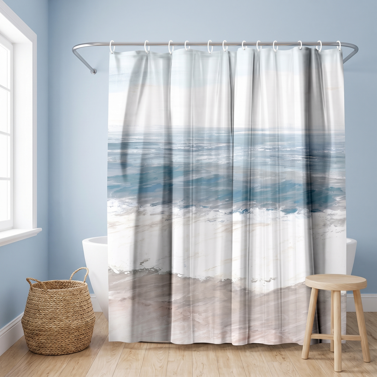 Shower curtain of soft teal sea, white surf and pale sand bands in a blue bathroom beside a freestanding tub and basket 