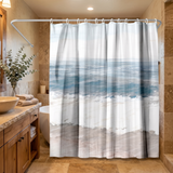 Shower curtain of soft teal sea, white surf and pale sand bands in a wood and stone bathroom beside folded towels 