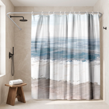 Shower curtain of soft teal sea, white surf and pale sand bands in a walk-in shower beside a black rain head and stool 