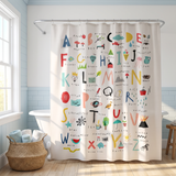 Shower curtain printed with a hand drawn A to Z alphabet chart in a bright white bathroom beside a tub and basket 