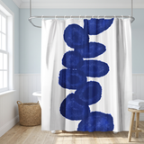 Shower curtain with a column of deep navy ink blots on white in a bright white bathroom beside a tub and basket 