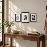 Three black frames with white mats above a walnut entryway console, with a small color digital photo in the center frame. 