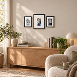 Three black frames with white mats above an oak cabinet beside a cozy reading chair. 