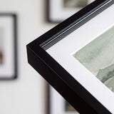 Close-up of the slim black molding, mitered corner, white mat and plexiglass 