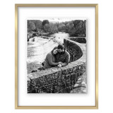 Gold metal float frame, a couple seated on a stone bridge above a weir 