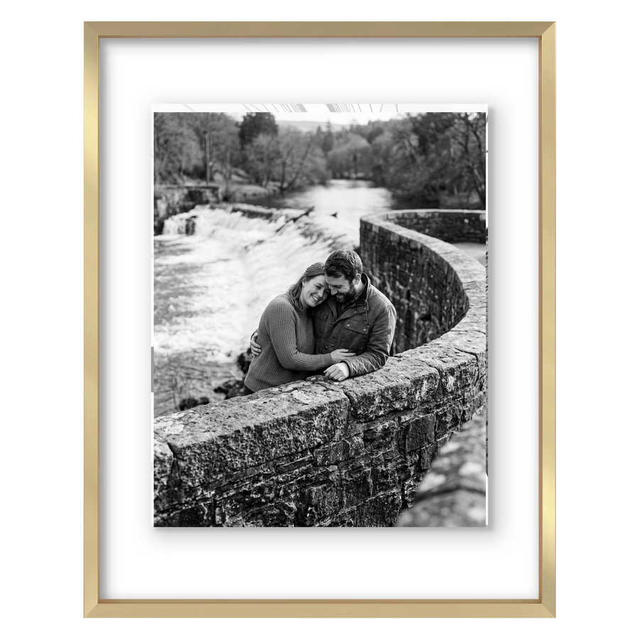 Gold metal float frame, a couple seated on a stone bridge above a weir 