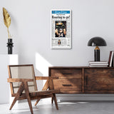White newspaper frame on a wall above a cane chair and a dark wood sideboard 