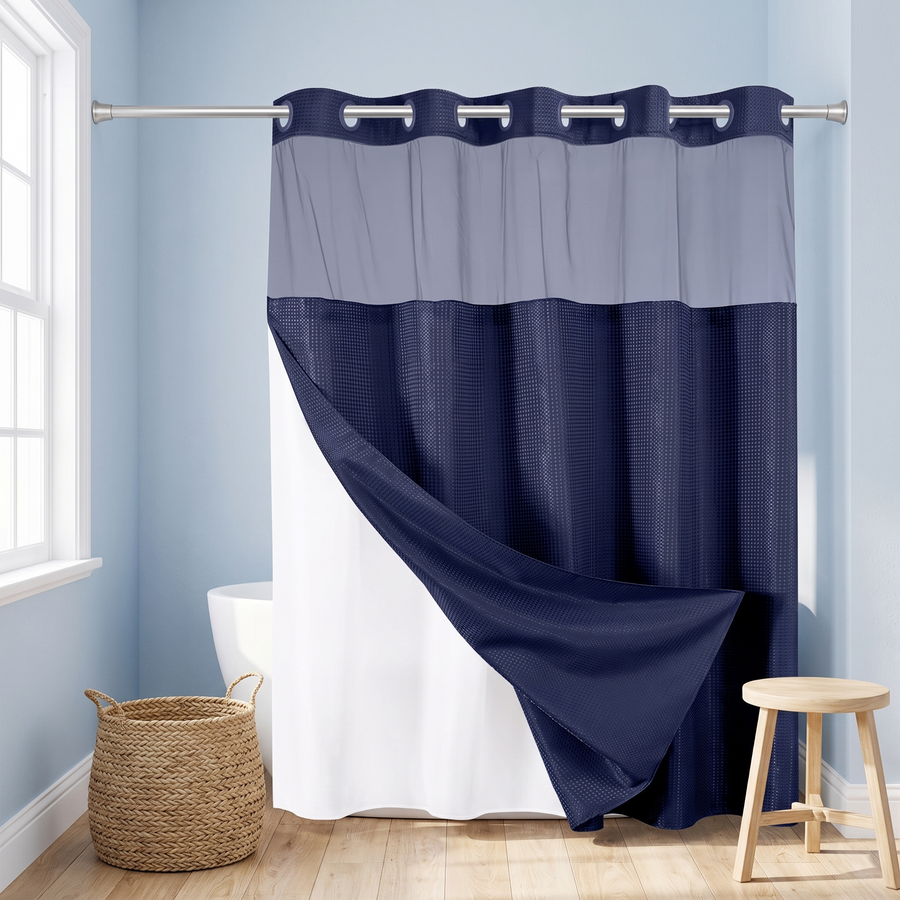 A two-tone shower curtain in navy blue and light gray, hanging on a silver rod in a bright bathroom with light blue walls, a window, a woven basket, and a wooden stool. 