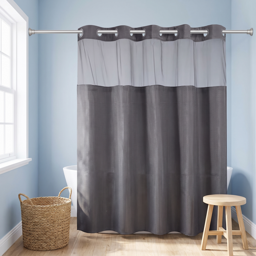 A two-tone gray shower curtain hanging from a silver rod in a bright bathroom with light blue walls, a window, a woven basket, and a wooden stool. 
