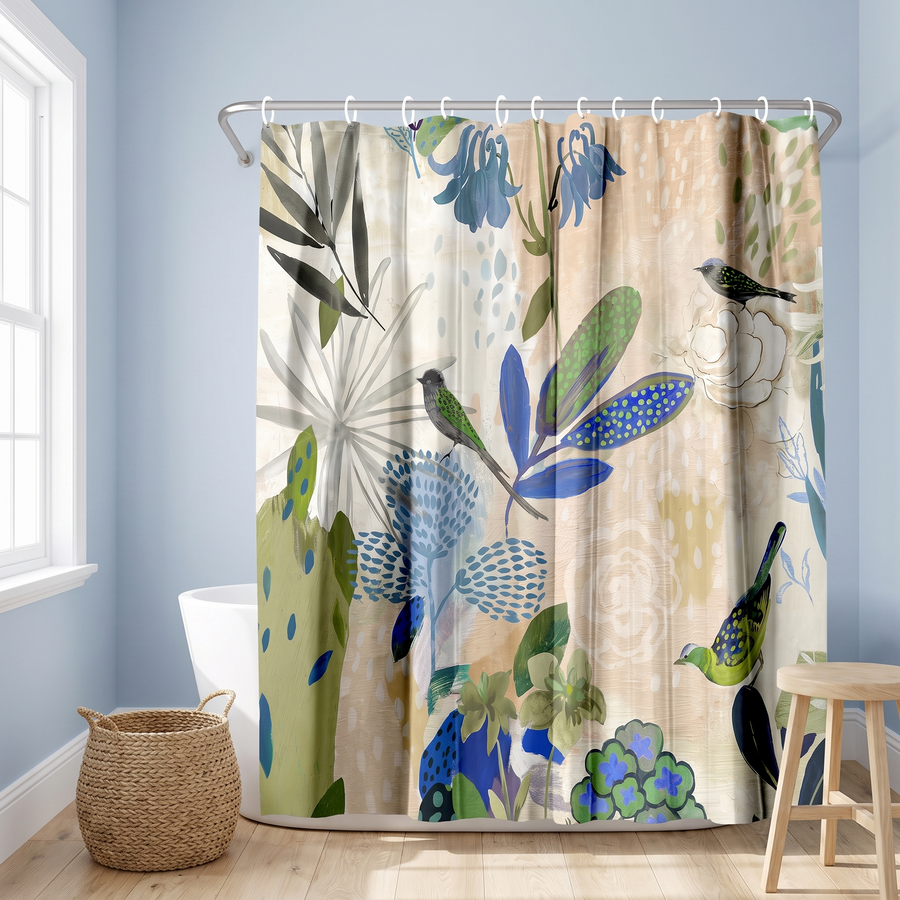 A fabric shower curtain hanging in a bathroom, featuring a botanical and bird pattern in blue, green, and beige tones. The scene includes a bathtub, window, woven basket, and wooden stool. 