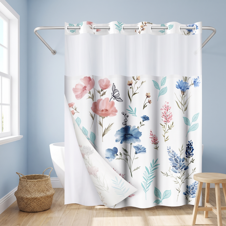 A white shower curtain with a watercolor-style floral print in pink, blue, and teal, hanging in a bathroom with light blue walls, a window, a woven basket, and a wooden stool. 