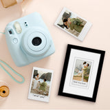 Black matted Instax frame beside a blue instant camera and loose instant prints 