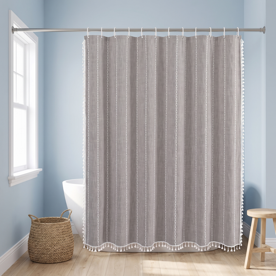 A gray and white patterned shower curtain hanging from a silver rod in a bright bathroom with light blue walls, a window, a woven basket, and a wooden stool. 