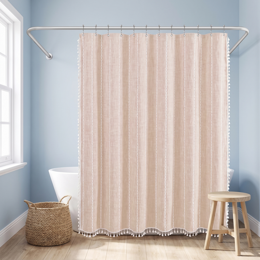 A beige shower curtain with vertical textured stripes and white tassel trim hanging in a bright bathroom with light blue walls, a bathtub, a woven basket, and a wooden stool. 