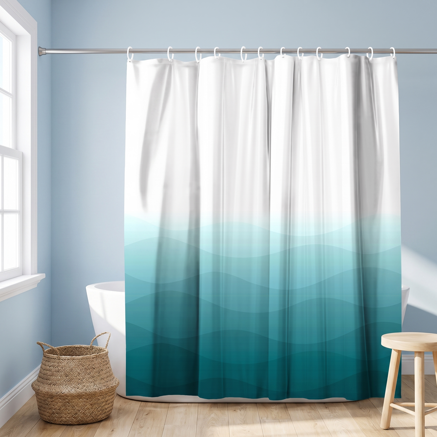A fabric shower curtain with a white-to-teal blue gradient and wavy pattern, hanging in a bathroom setting with a bathtub, wooden stool, and woven basket.  