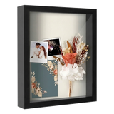 Black 11x14 shadow box holding a wedding photo, dried flowers and an invitation 