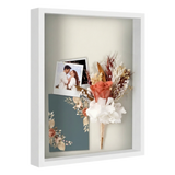 White 16x20 shadow box holding a wedding photo, dried flowers and an invitation 