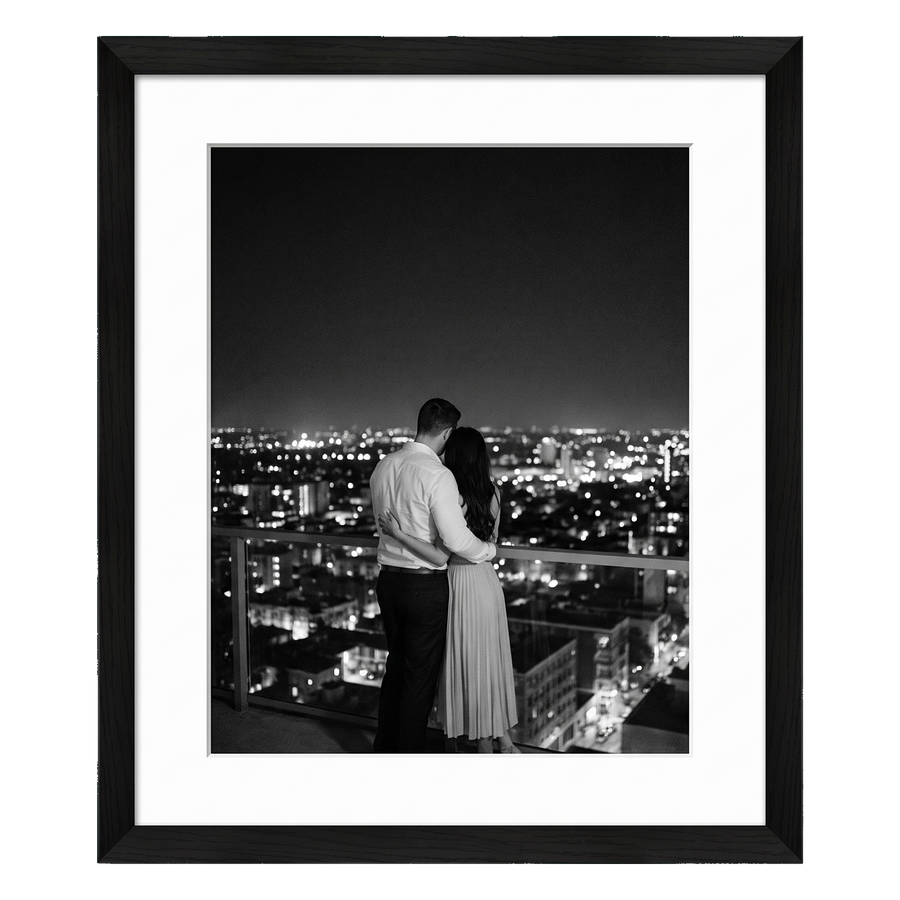 Black Hudson frame, 18x24, with a 12x18 white mat, holding a black-and-white photo of a couple above city lights at night 