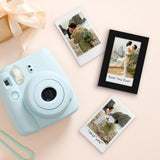 Black Instax frame beside a blue instant camera and loose prints on a pale surface 
