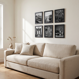 Six black picture frames in a grid above a linen sofa in a bright living room 