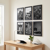 Six black picture frames in a grid above an oak desk in a home office 