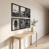 Six black picture frames in a grid above a console table in a sunlit entryway 