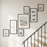 Ascending stairway gallery wall of seven black frames climbing alongside a staircase
