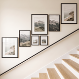 Balanced seven-frame black gallery wall on a staircase, glazed frames catching soft daylight