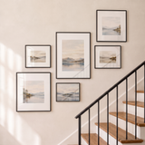 Six-frame mixed-size black gallery wall with two square frames, glazed and catching soft daylight