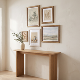 The five-frame collected gallery hung above an oak console table in a sunlit entryway 