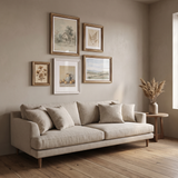 The five gold and white frames grouped above a low linen sofa in a warm living room 