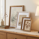 Gold and white Heirloom frames layered and leaning on a wooden sideboard in lamp light 