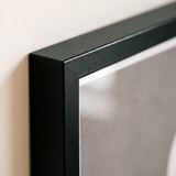 Close-up of the black poster-frame corner, unmatted with the print running to the moulding 