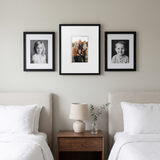 The three-frame digital set styled above a walnut nightstand in a bedroom, the digital frame glowing softly between two black-and-white portraits 