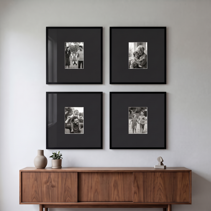 Wide Mat Grid Four 16x16: four black Streamline 16x16 frames with black 5x7 mats, hung as a two-by-two square. Shown in a modern living room, above a low walnut credenza, with family photos in the frames 