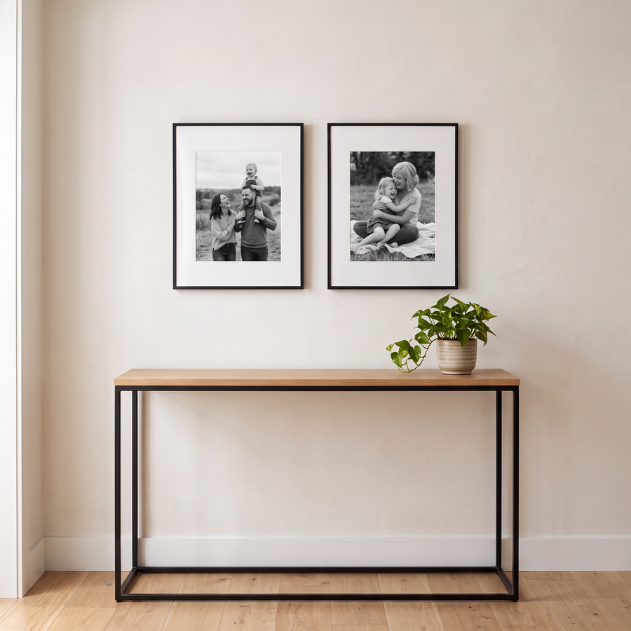 Brooklyn Duo: two black Brooklyn aluminium 11x14 frames matted to 8x10, hung side by side. Shown in a hallway, above a narrow console table with a small plant, with family photos in the frames 