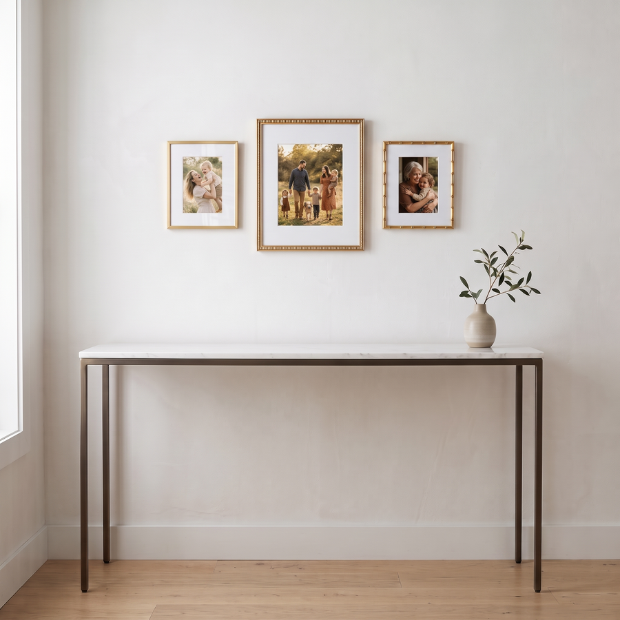 Three Golds Trio: three gold frames in three styles (Heirloom 11x14, Streamline 8x10, Memento 8x10), in one row; all matted. Shown in an entryway, above a marble-topped console table with a vase, with family photos in the frames 
