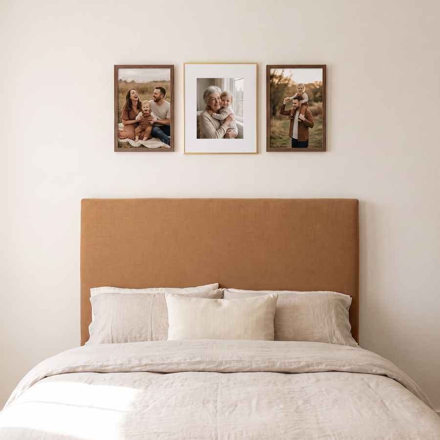 Walnut & Gold Trio: a matted gold Brooklyn 16x20 between two unmatted walnut 12x18 Signature frames, in one row. Shown in a warm bedroom, above a bed with a caramel upholstered headboard, with family photos in the frames 