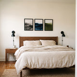 Three black 12x17 unmatted poster frames in a row above a walnut queen headboard, true to size 