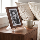 4-inch clear acrylic display stand holding a small black-and-white photo in a dark wood frame on a walnut nightstand 