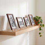 Four clear acrylic display stands in a row on a floating oak shelf holding black-and-white photographs 