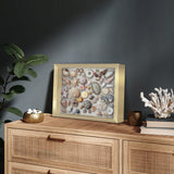 Gold shadow box of seashells on a cane sideboard against a dark wall beside coral 